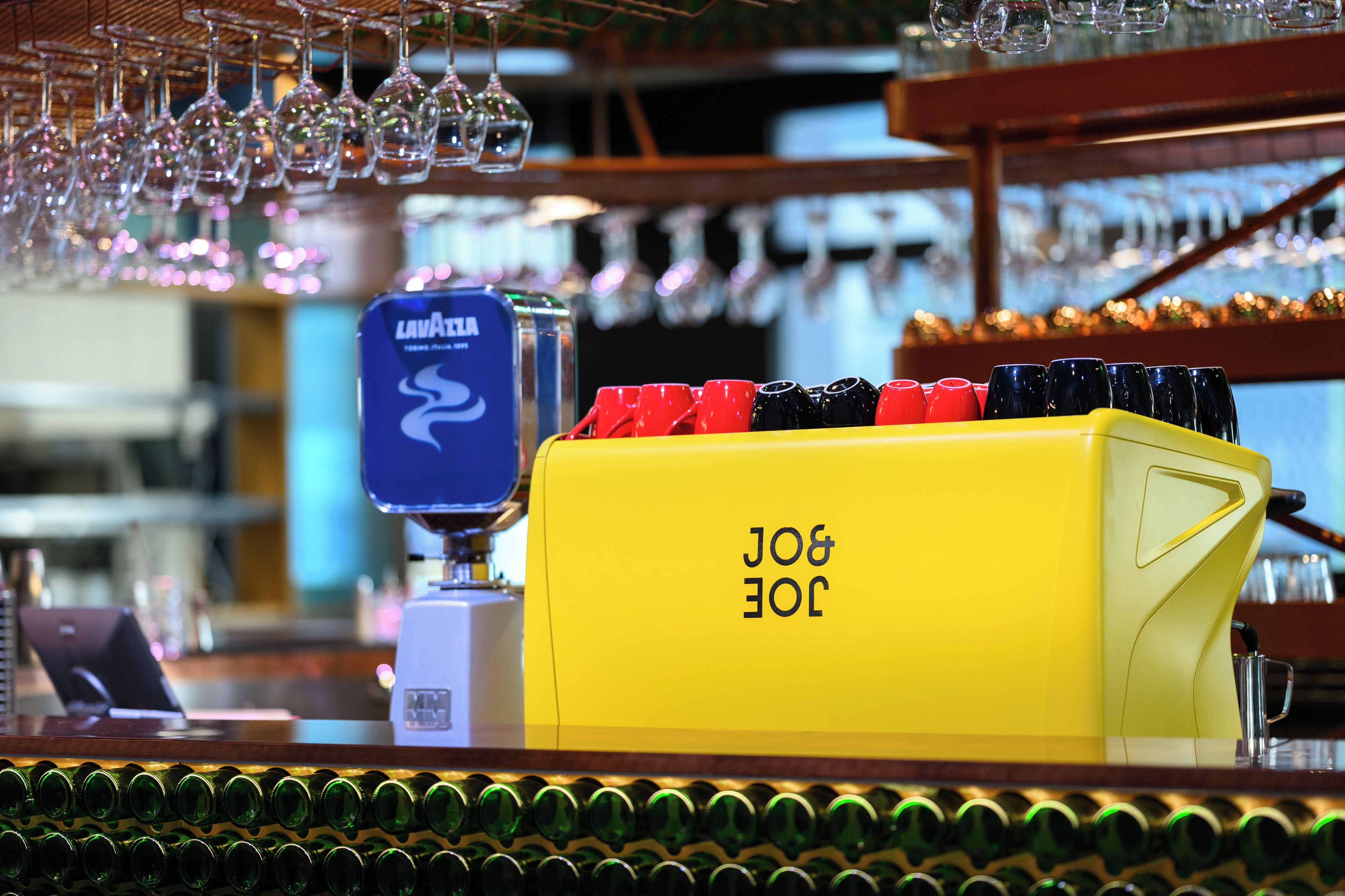 A bar area with a yellow tap labeled 'LAVAZZA' and a row of colorful glasses.