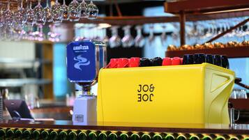 Zona de bar con un grifo amarillo etiquetado 'LAVAZZA' y una fila de vasos de colores.