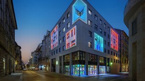 A modern building with a unique geometric facade and illuminated windows at dusk. - JO&JOE Budapest (Budapest)