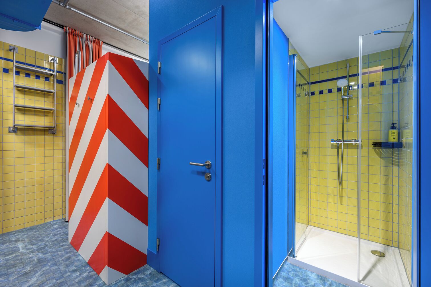 A bathroom with a blue door, yellow tiled walls, and a glass shower enclosure.