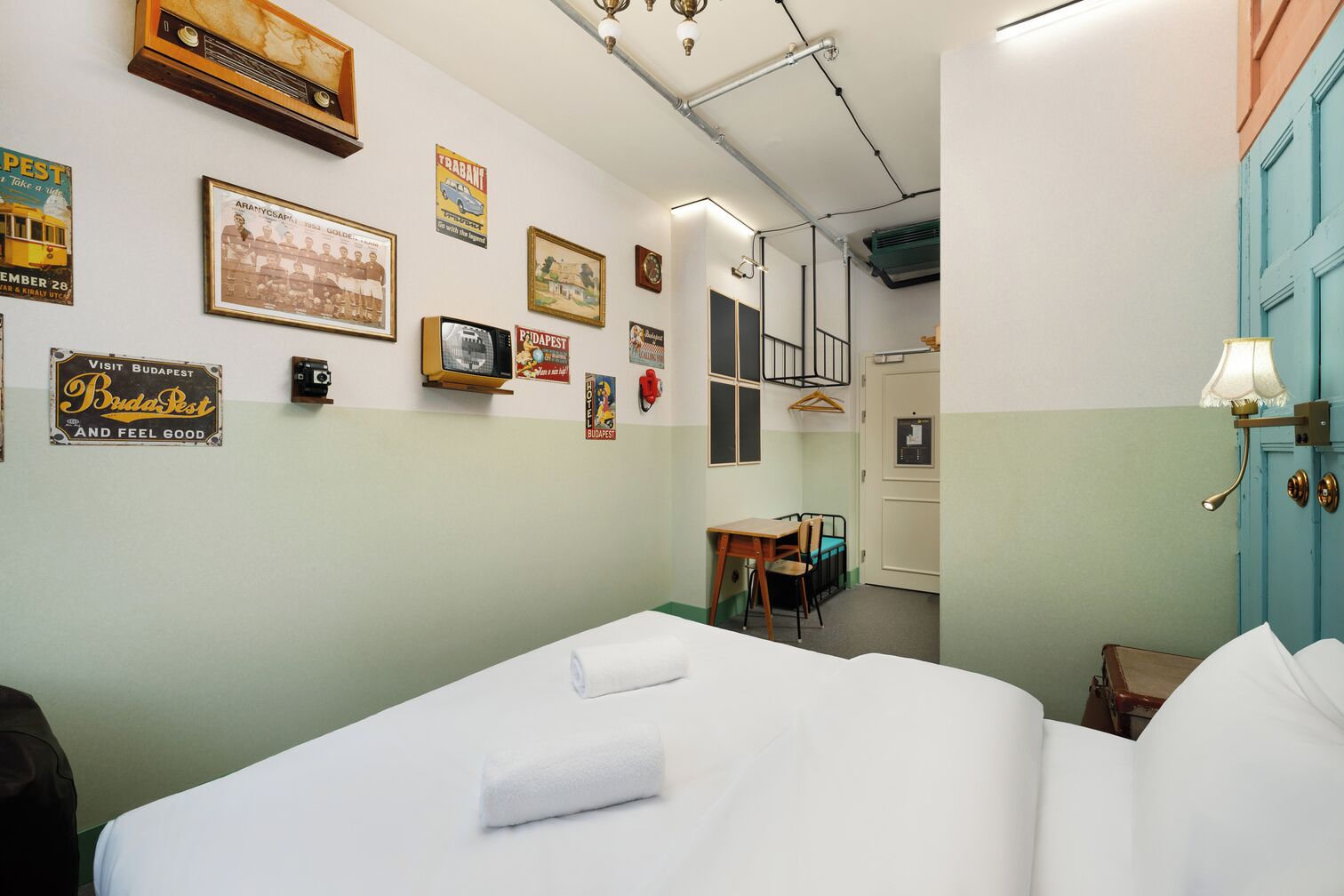 A hotel room with a bed, a desk, a chair, and a blue door.