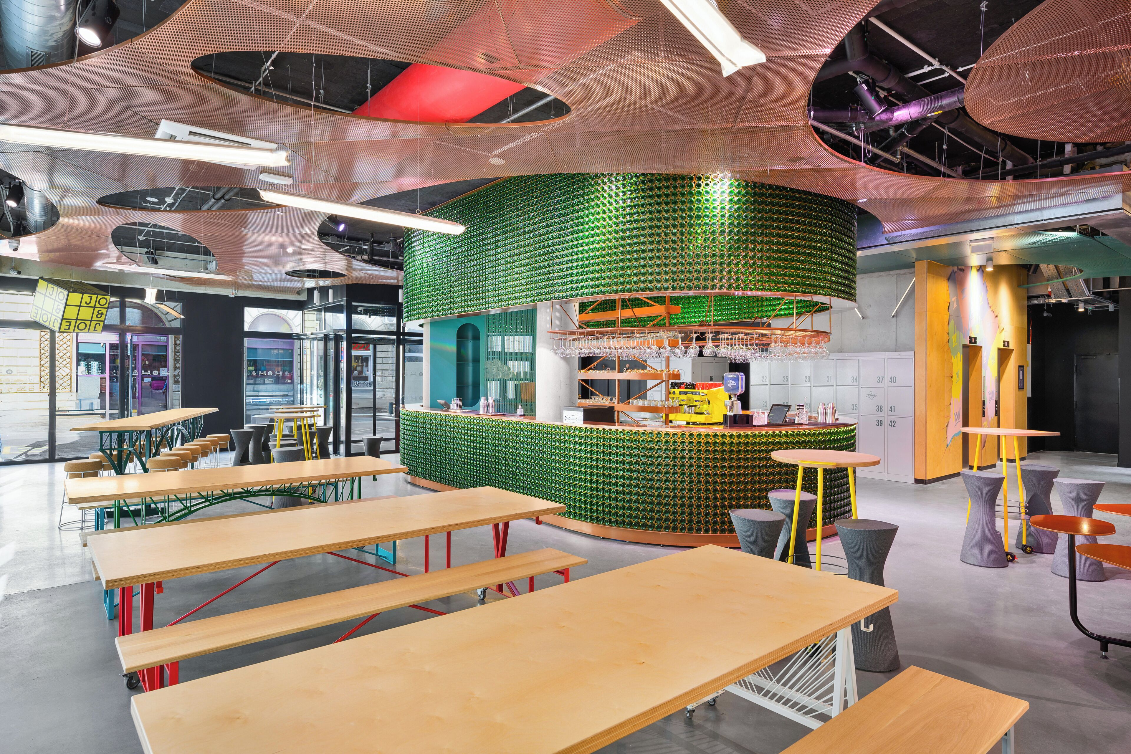 A modern interior with a green bottle wall, wooden tables, and a bar area.