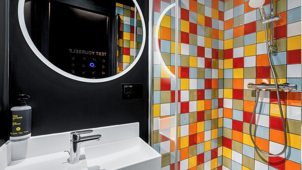 A bathroom with a white sink, a mirror, a handheld showerhead, and a colorful tiled wall. - JO&JOE Budapest (Budapest)