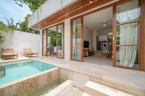 A modern house with a swimming pool, wooden deck, and large sliding glass doors leading to a living area with a TV and furniture. - Villa Lilu  (Canggu)