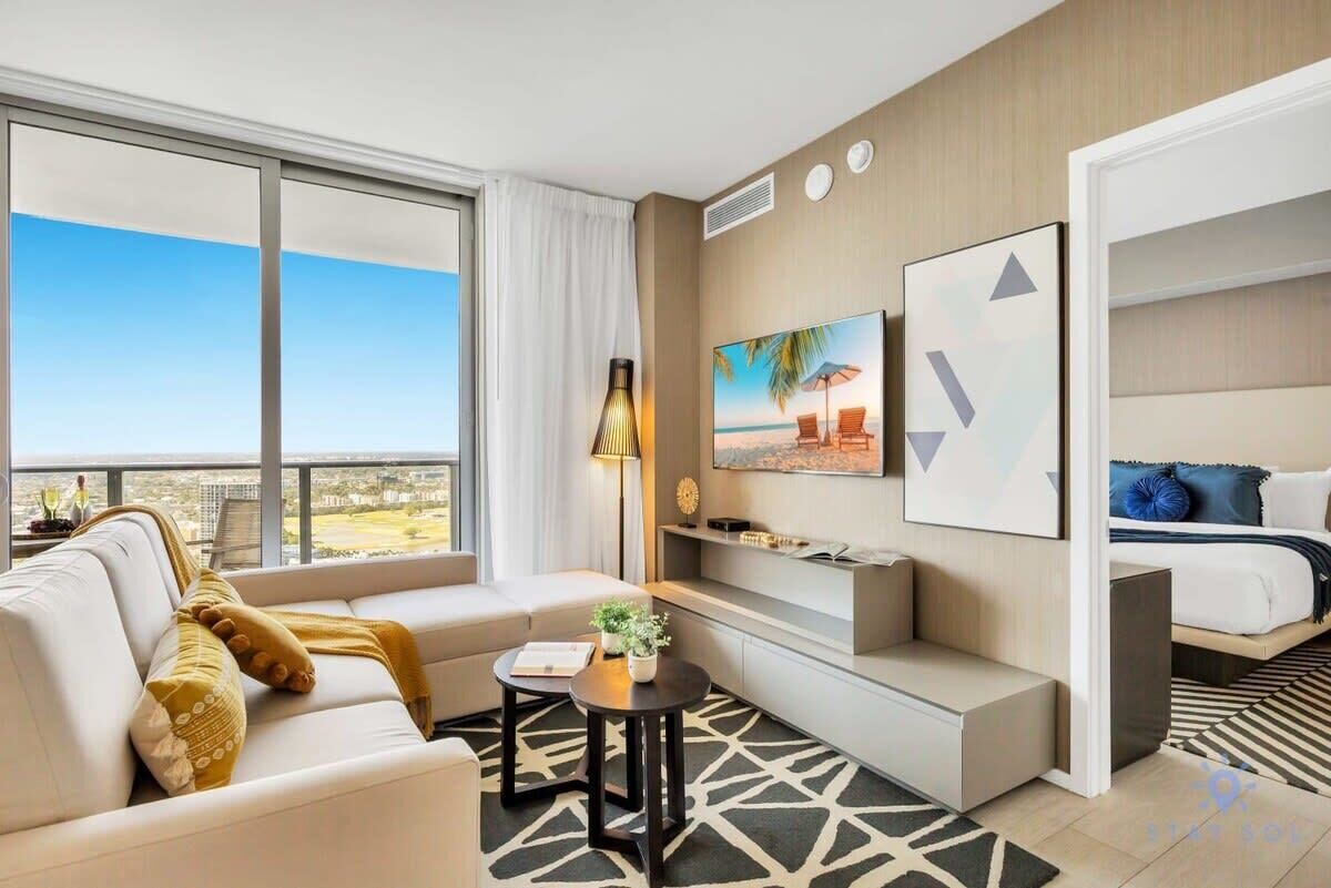 Ein modernes Hotelzimmer mit einer Couch, einem kleinen Tisch, einem Bett und einem großen Fenster mit Blick auf die Stadt.