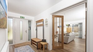 A modern interior with a wooden floor, a white door, a small table, a bench, and a sofa in the background. - Tre Lowen- Enclosed Garden - Free Parking (Perranporth)