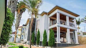 A modern two-story building with a balcony, surrounded by well-maintained landscaping and palm trees. - Net Luna Villa Hotel and Tours  (Kigali)