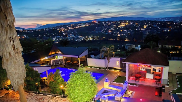 A rooftop pool area with a restaurant, surrounded by landscaped gardens and a view of a cityscape at dusk. - Net Luna Villa Hotel and Tours  (Kigali)