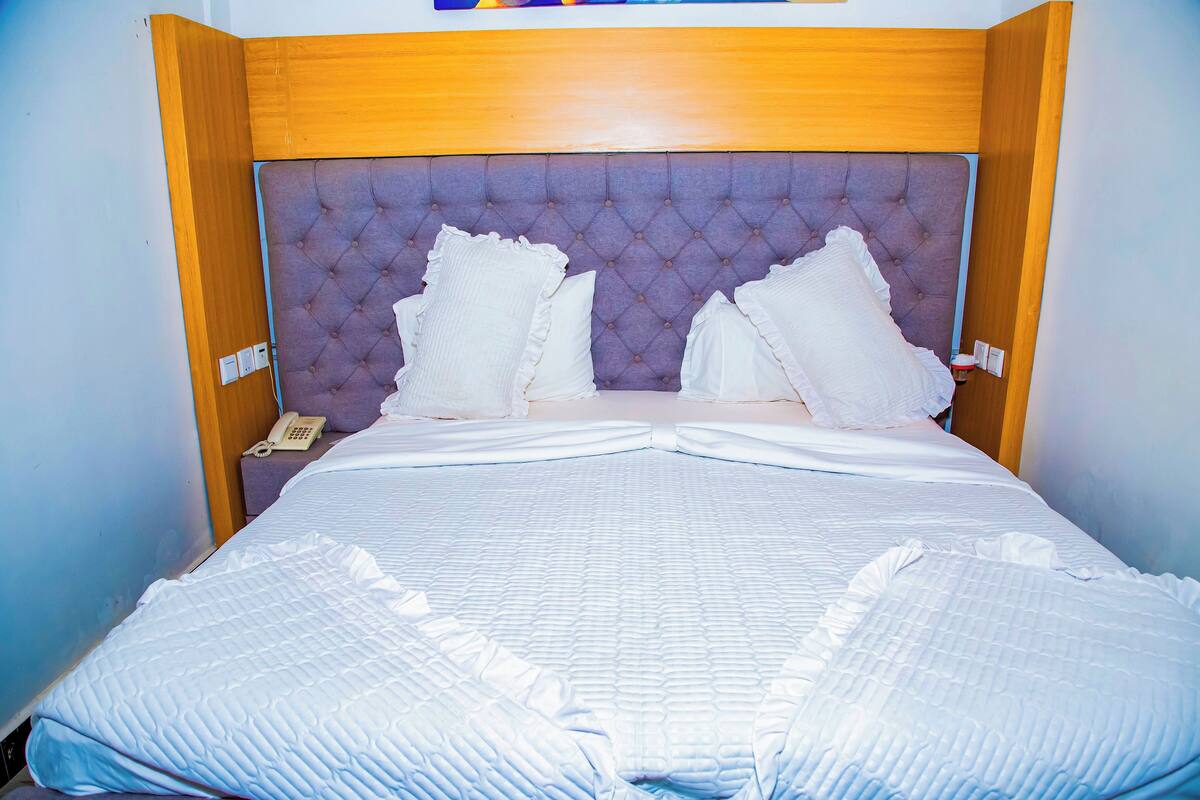 A neatly made bed with a tufted headboard, white bedding, and a bedside telephone.