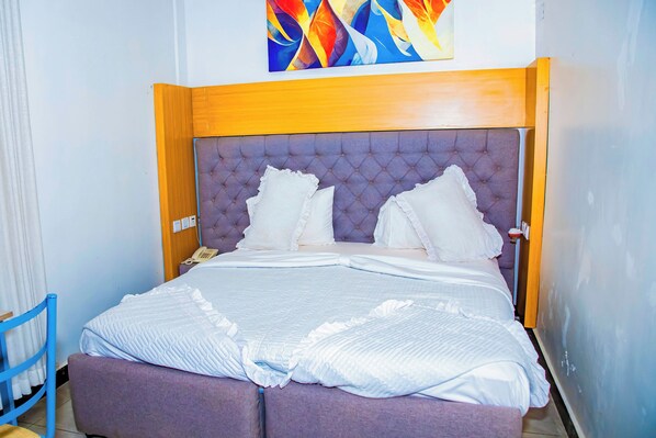 Una cama bien hecha con un cabecero capitonado, un teléfono en la mesita de noche y un cuadro abstracto de colores sobre ella.
