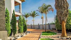 A paved pathway leading to a building with a balcony, surrounded by palm trees and cypress trees. - Net Luna Villa Hotel and Tours  (Kigali)