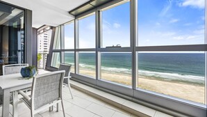 A balcony with a view of the ocean, a dining table with chairs, and a potted plant.