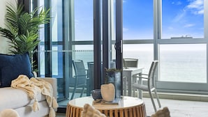 A modern living room with a sofa, a round wooden coffee table, and a view of the ocean through large windows.