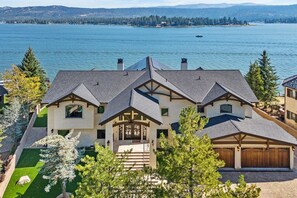 Ein großes, mehrstöckiges Haus mit einer auffälligen Veranda und einer Garage, am See gelegen mit freiem Blick auf das Wasser.