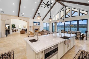 A spacious kitchen with a large island, a fireplace, and a view of a lake. - Waterfront Dreams: Luxurious Lakefront! Incredible Views! 5 Masters! A/C! Extravagant Outdoor Living! Hot Tub! Pool Table and more! (Fawnskin)