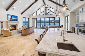 A spacious living area with a fireplace, seating, and a large window overlooking a body of water. - Waterfront Dreams: Luxurious Lakefront! Incredible Views! 5 Masters! A/C! Extravagant Outdoor Living! Hot Tub! Pool Table and more! (Fawnskin)