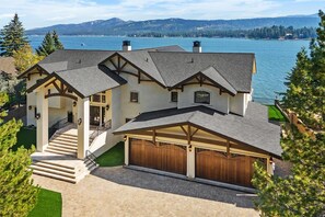 A large house with a covered garage, a staircase leading to the entrance, and a view of a lake. - Waterfront Dreams: Luxurious Lakefront! Incredible Views! 5 Masters! A/C! Extravagant Outdoor Living! Hot Tub! Pool Table and more! (Fawnskin)