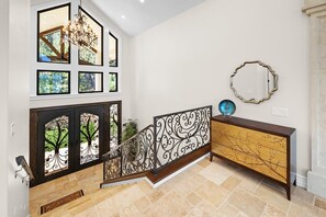Una escalera con barandilla decorativa, una consola de madera con un espejo y cuadros enmarcados en la pared.