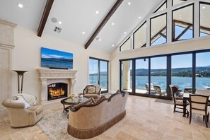 A spacious living room with a fireplace, comfortable seating, and a large window overlooking a lake.