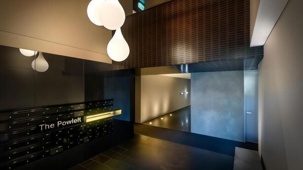 Un espace d’accueil moderne avec un comptoir noir portant l’inscription « The Powelt », un éclairage d’ambiance et un design contemporain.