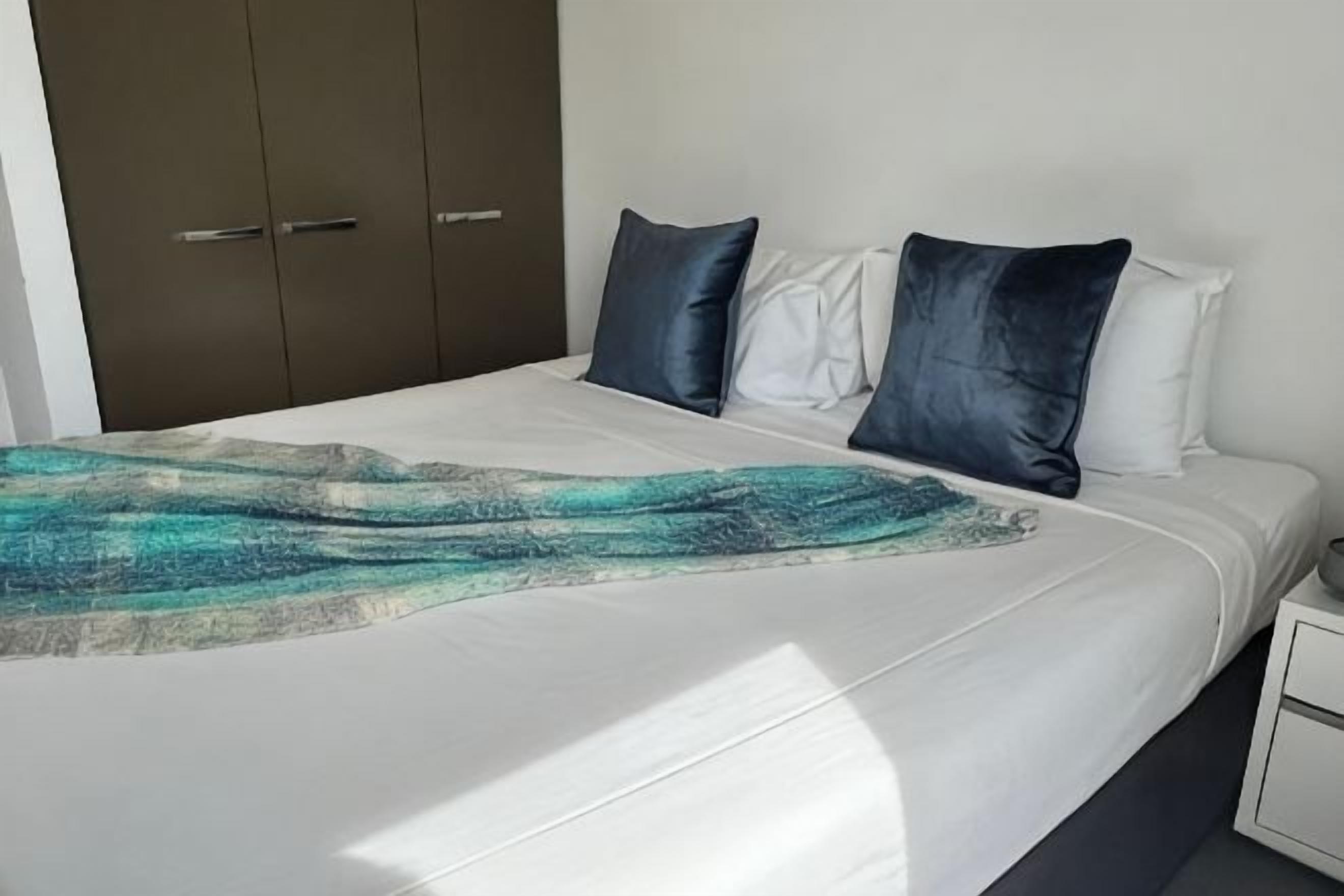 Un letto con lenzuolo bianco, due cuscini e una coperta.