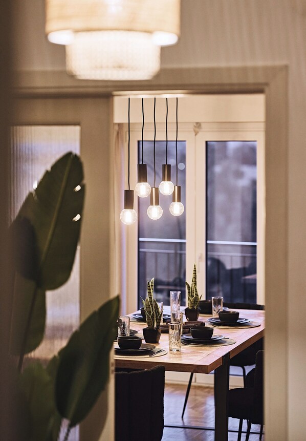 A dining area with a wooden table set for two, hanging pendant lights, and potted plants. - Kova Residence, Acropolis by Aura Homes (Athens)