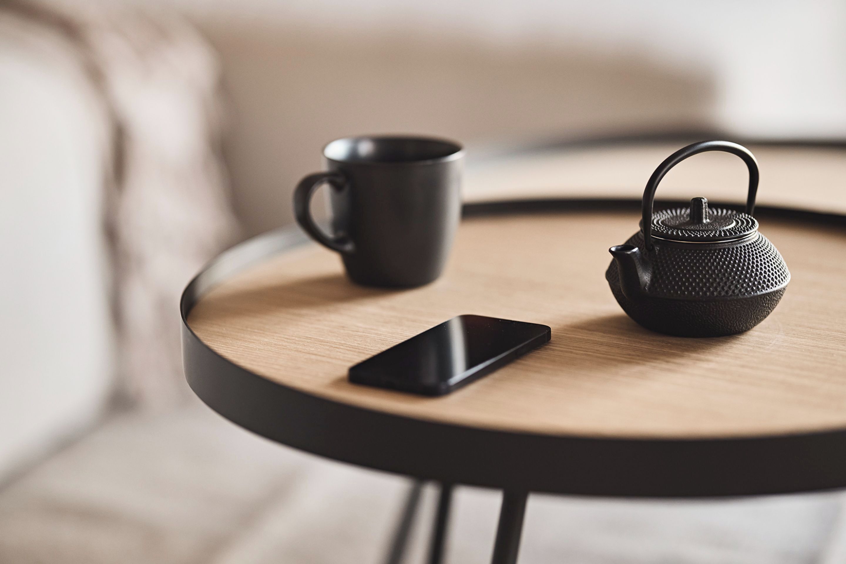 A round wooden table with a black teapot and a black mug on it.