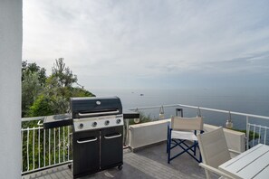 Eine Terrassenanlage im Freien mit Grill, weißen Stühlen und Meerblick.