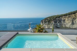 Une piscine à débordement située sur le toit, offrant une vue dégagée sur la mer et une falaise.
