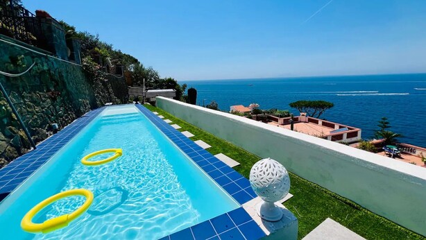 Ein Pool mit Blick auf das Meer, eine weiße, kugelförmige Leuchte und eine Steinsäule.