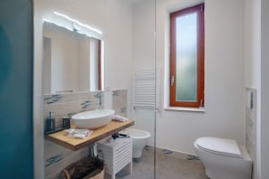 Ein modernes Badezimmer mit großem Spiegel, Waschbecken in Weiß, Toilette und Duschkabine aus Glas.
