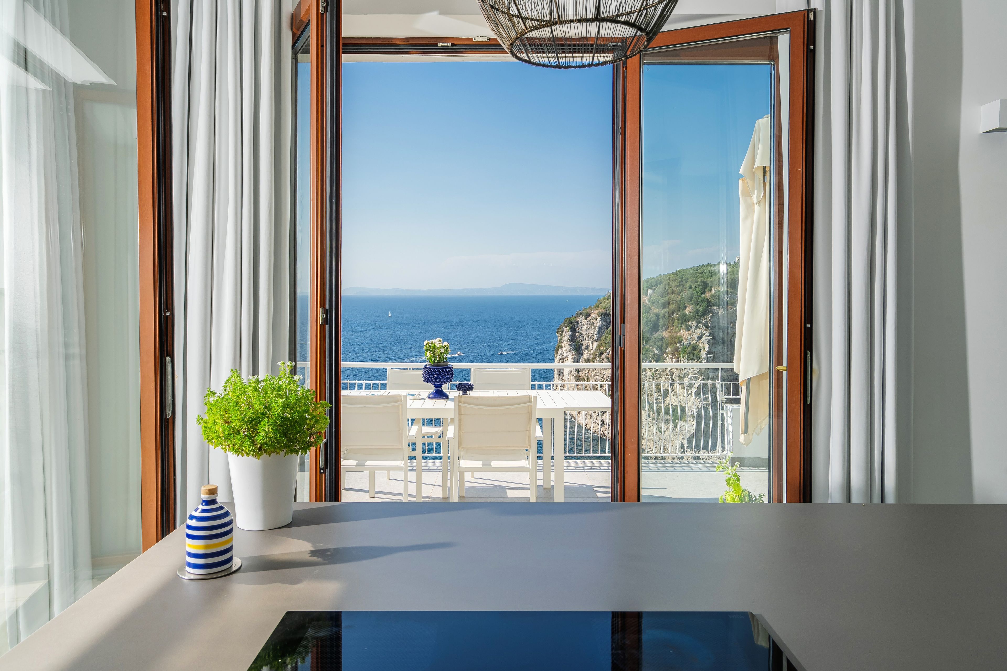 A balcony with a view of the sea and a table with chairs and a potted plant.