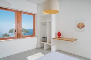 Un dormitorio con un ventanal grande, una cama, una lámpara colgante y un estante con un objeto decorativo.