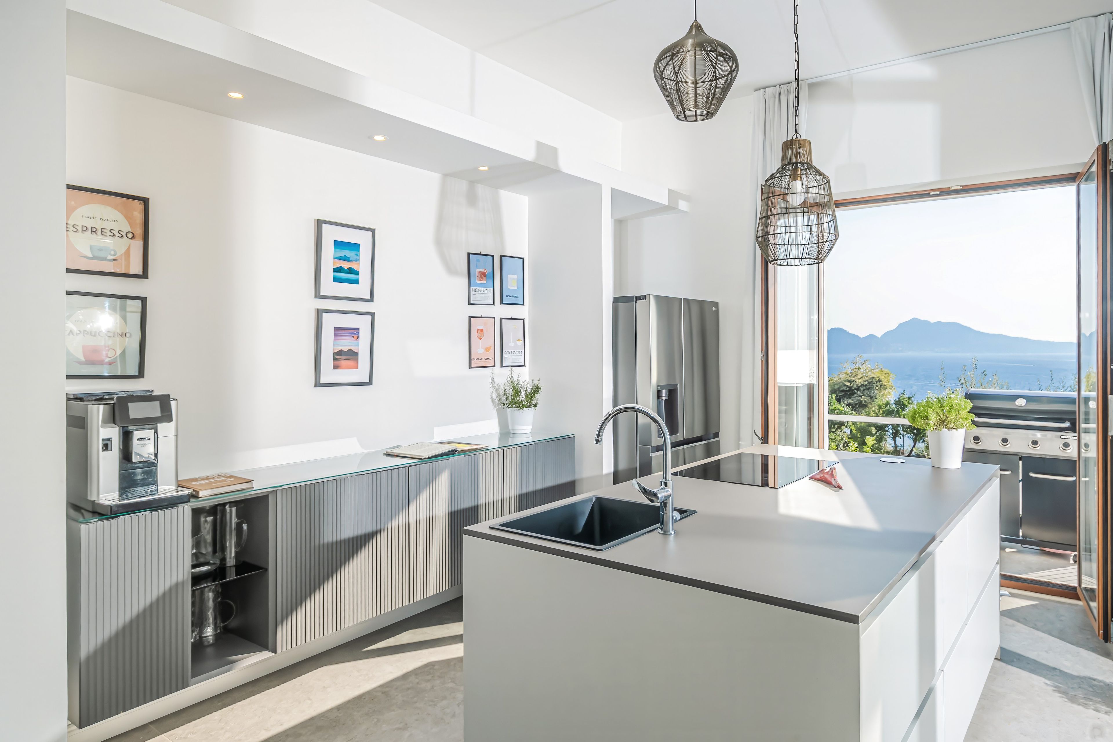 A modern kitchen with a central island, stainless steel appliances, and a view of the sea.