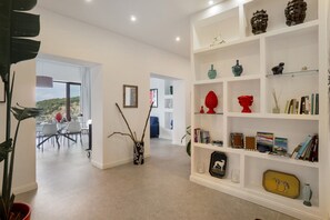 A modern living room with a white bookshelf, a dining area with a view, and a large plant.