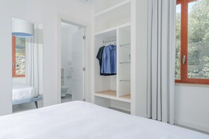 Une chambre à coucher avec un lit, une armoire où sont suspendus des vêtements, et une salle de bain avec des toilettes et un bidet.