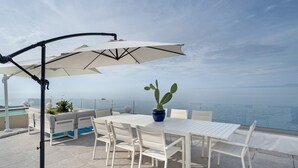 Eine Terrasse mit Tisch, Stühlen, einem Topfpflanzen und einem großen Sonnenschirm.