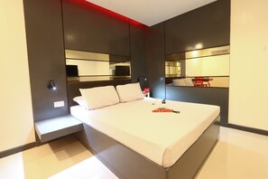 Une chambre d’hôtel moderne avec un grand lit, des tables de chevet, un miroir et un mur d’accent rouge.