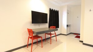 Ein modernes Zimmer mit einem an der Wand befestigten Flachbildfernseher, einem kleinen Tisch mit zwei roten Stühlen, einem schwarzen Vorhang und einem roten Teppich.