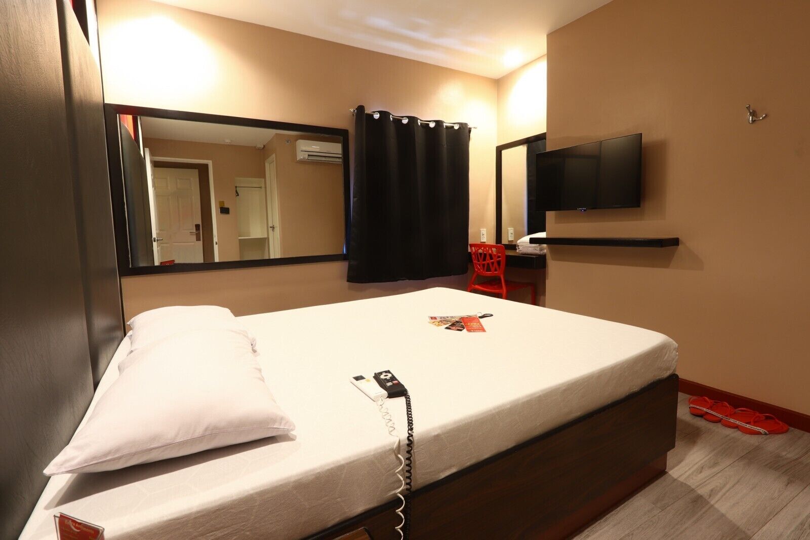 Een hotelkamer met een bed, een aan de muur bevestigde televisie, een spiegel en een douchegordijn.