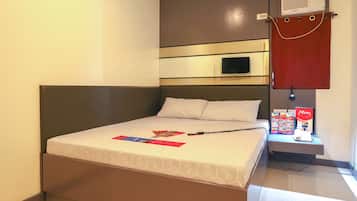 A hotel room with a bed, a flat-screen TV, a red curtain, and a minibar.