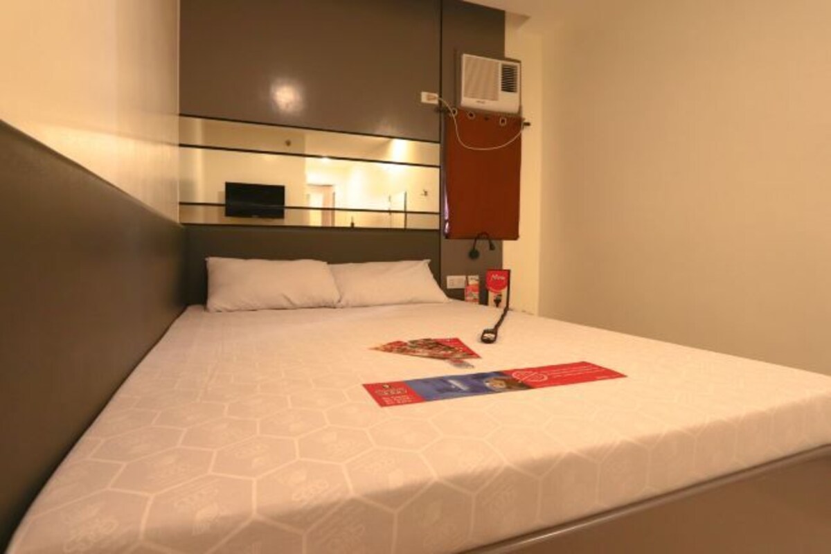 Een hotelkamer met een bed, een wandairconditioner en een nachtkastje met een lamp.