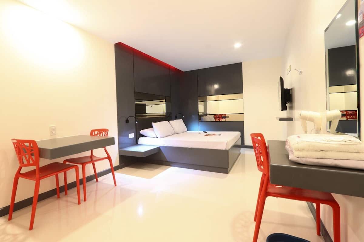 A modern bedroom with a bed, a desk, and two red chairs.