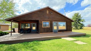 A wooden cabin with a covered porch, large windows, and a view of the surrounding landscape.