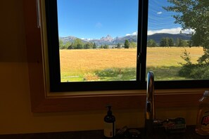 Une fenêtre donnant sur un champ et des montagnes.
