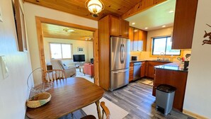 A modern kitchen with wooden cabinets, a stainless steel refrigerator, and a dining area with a wooden table and chairs.