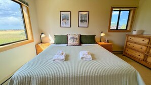 A neatly made bed with two towels, a wooden nightstand with a lamp, a dresser, and two framed pictures on the wall.