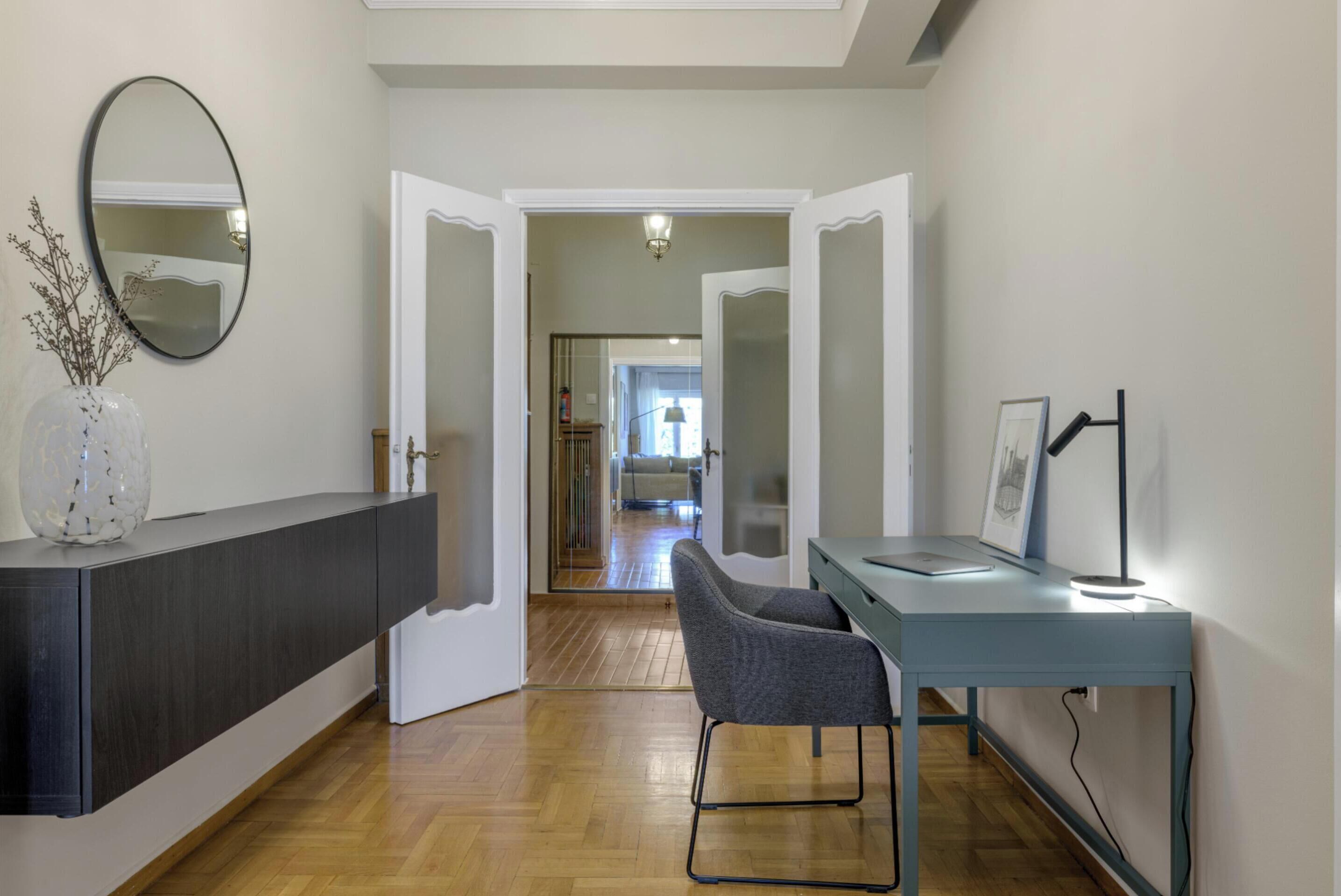 A modern interior with a dark wood console, a grey chair, and a desk with a lamp.