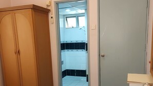 A bedroom with a wooden wardrobe, a door leading to a bathroom, and a bed with white bedding. - Glory by Alpine (Port Dickson)