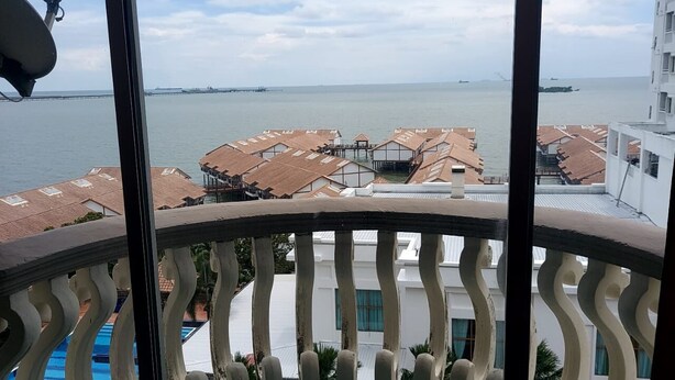 A balcony with a view of a coastal area, featuring buildings with red-tiled roofs and a body of water in the background. - Glory by Alpine (Port Dickson)